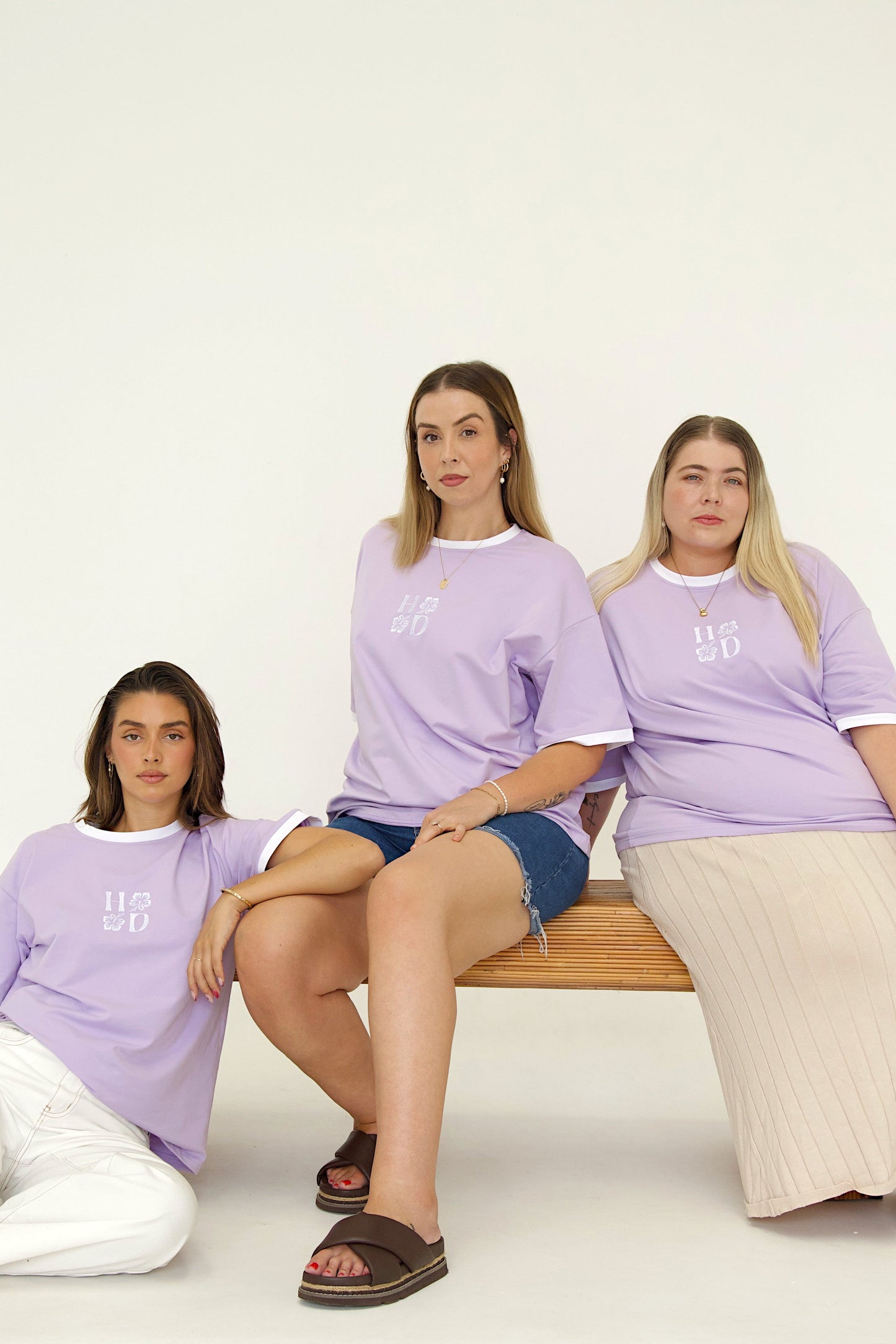Three women wearing matching purple t-shirts sitting on a white background