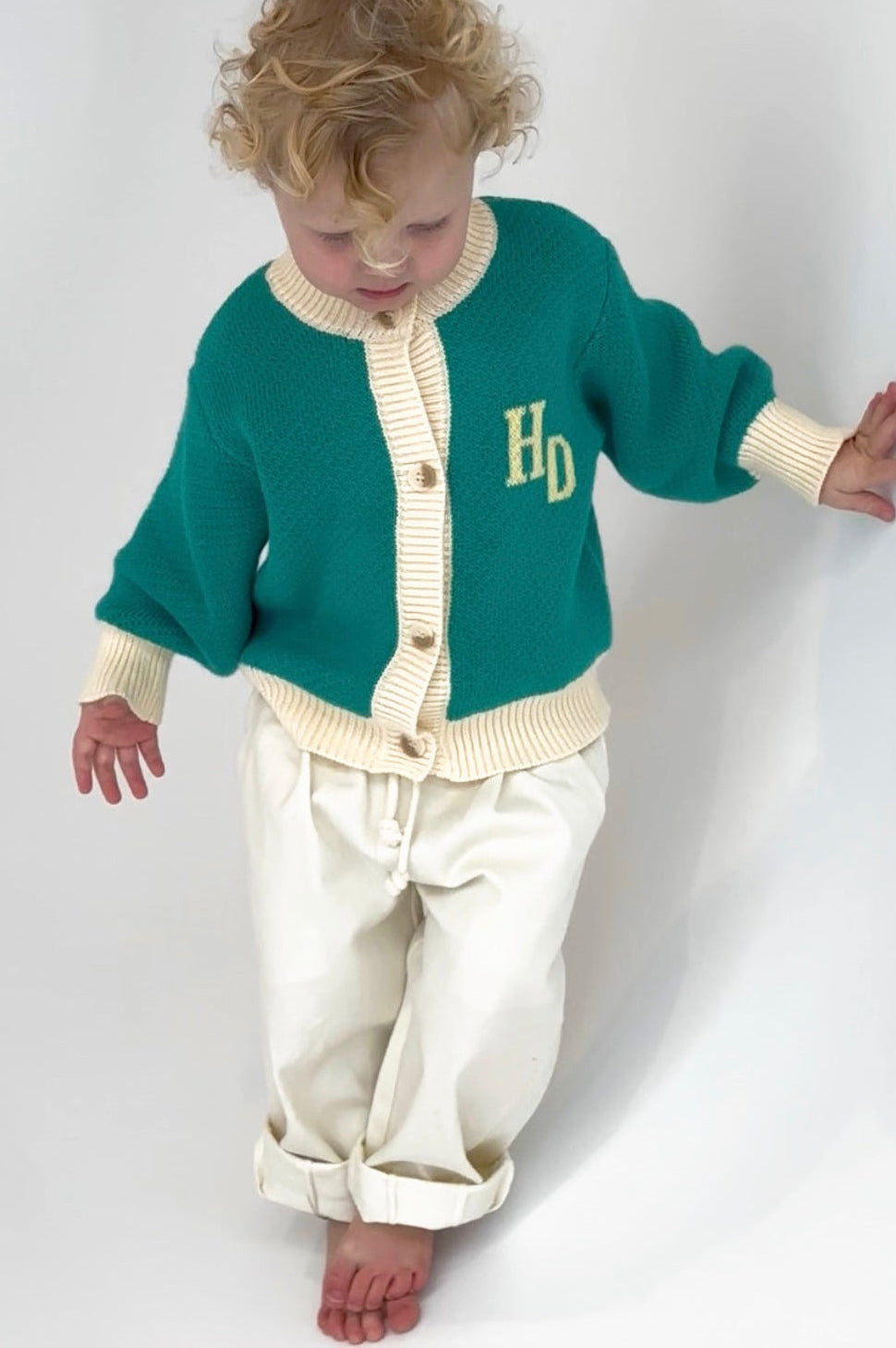 Child wearing a green cardigan with 'HD' initials on a white background