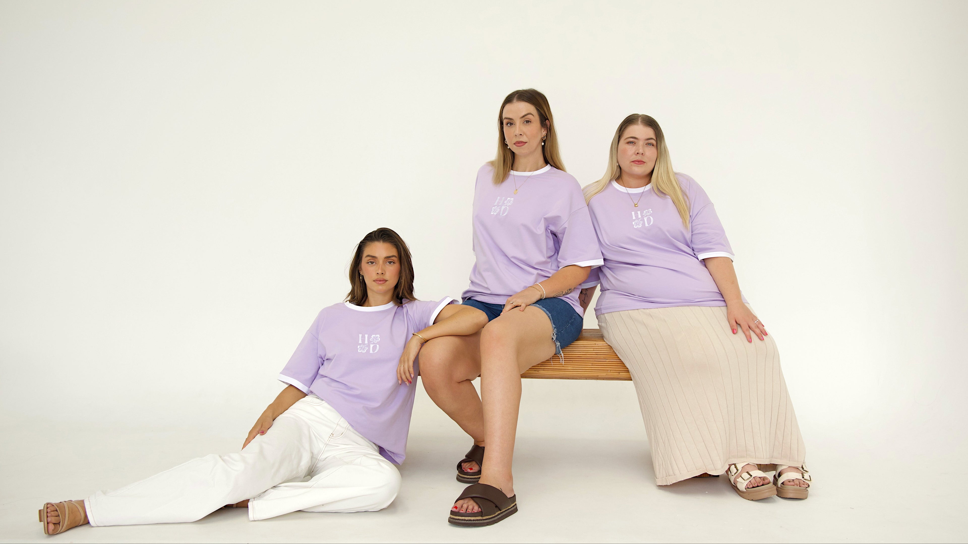 Three women wearing matching purple t-shirts sitting on a white background